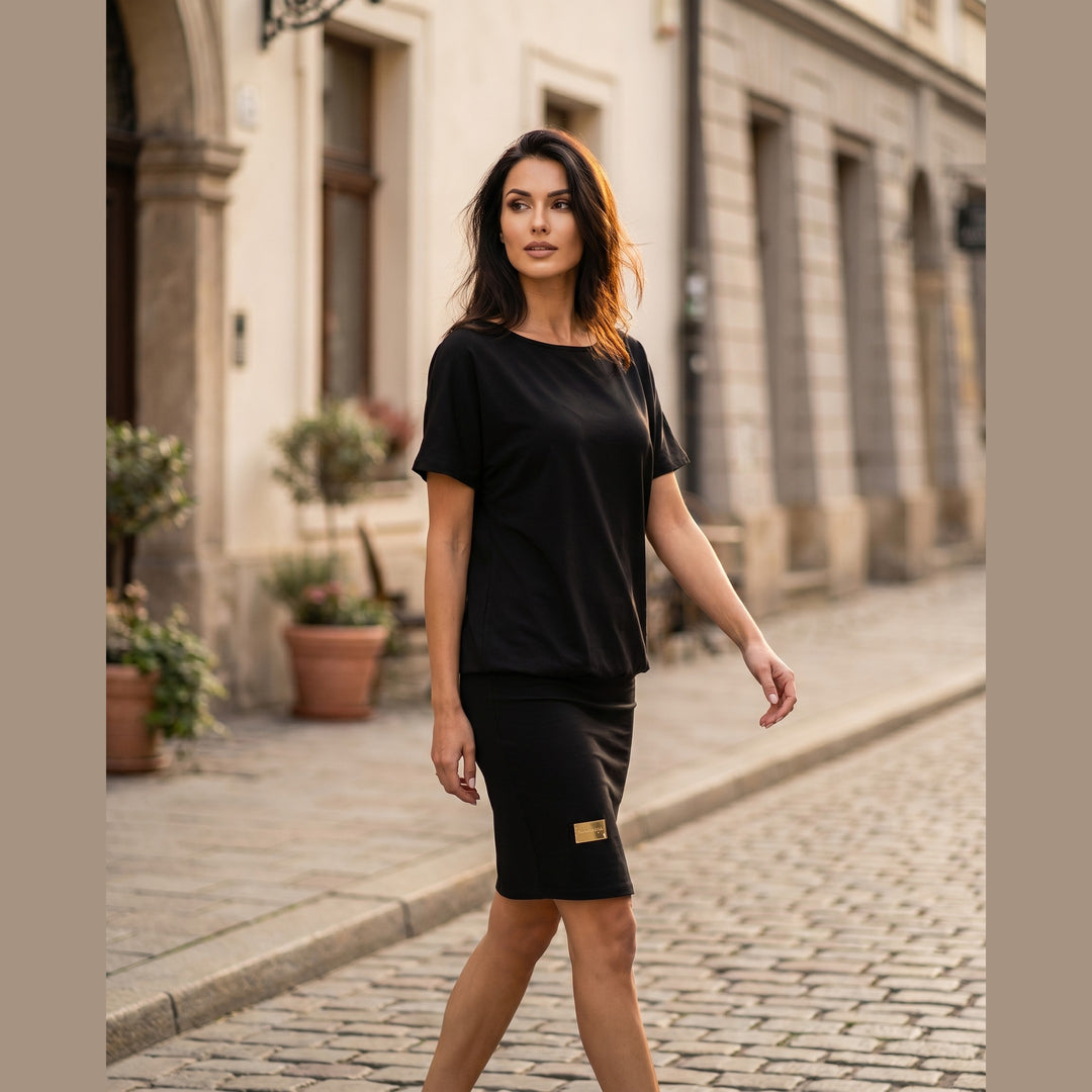 Woman wearing the black Melissa relaxed stretch dress, walking on a sunlit street