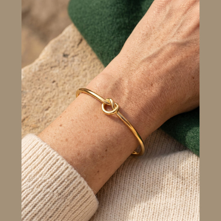 Minimal knot cuff bracelet in gold worn on a woman's wrist